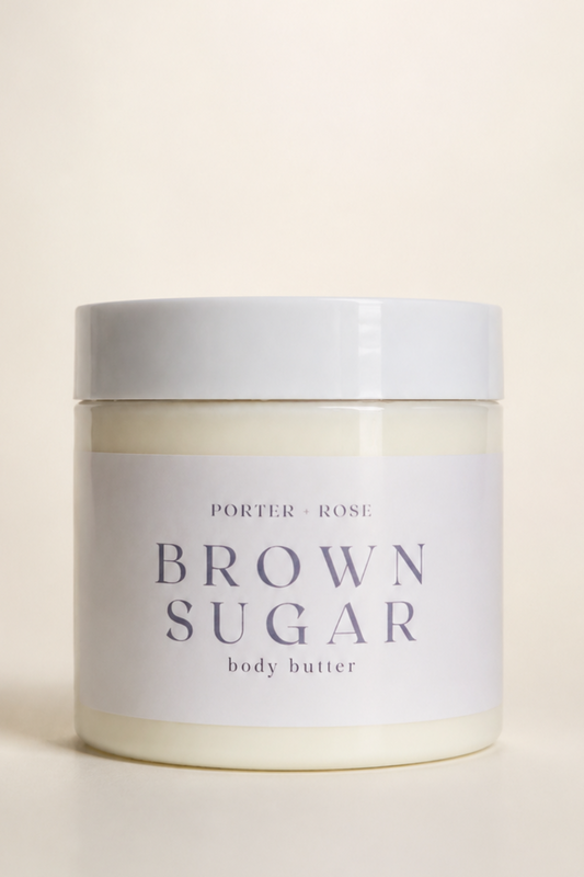A jar of porter ROSE Brown Sugar body butter, featuring a white label with dark gray text and a matching white lid, set against a warm cream background.