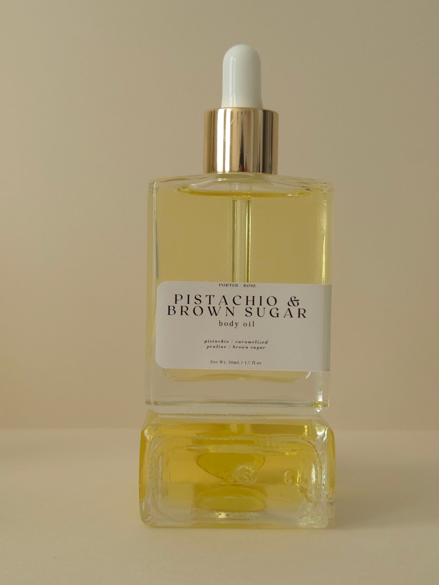 Bottle of 'Pistachio & Brown Sugar' body oil on a beige background