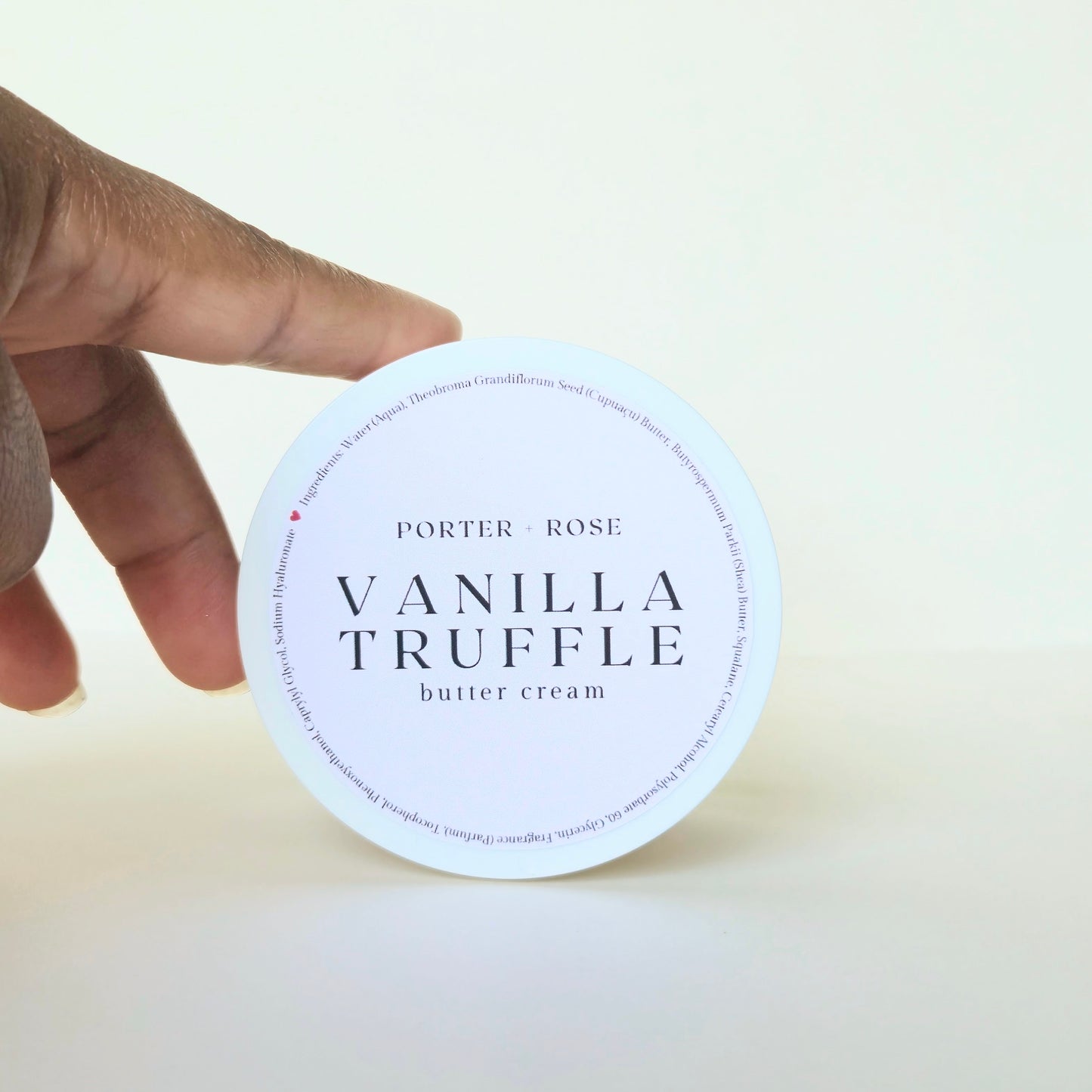 Hand holding a container of Porter & Rose Vanilla Truffle body butter cream against a white background