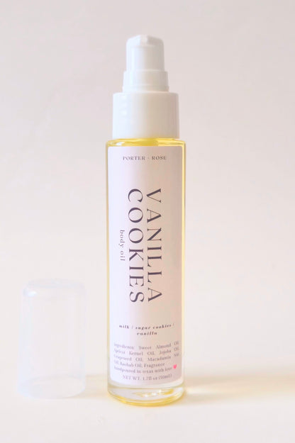 A bottle of Vanilla Cookies body oil with a white pump dispenser and a translucent cap resting beside it on a clean, light beige background.