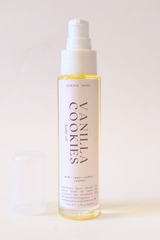 A bottle of Vanilla Cookies body oil with a white pump dispenser and a translucent cap resting beside it on a clean, light beige background.