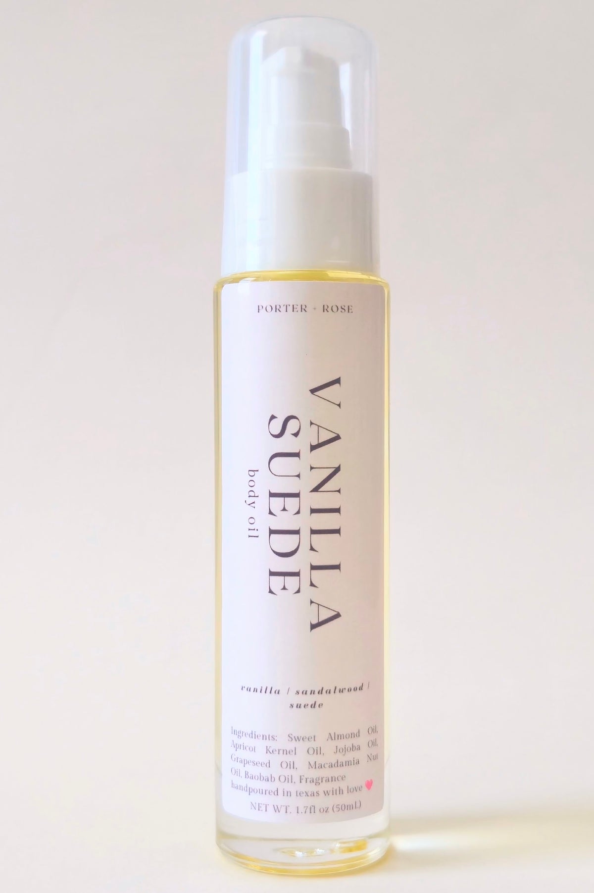 A bottle of Porter Rose Vanilla Suede body oil with a white spray cap and a cream-colored label, set against a plain off-white background.