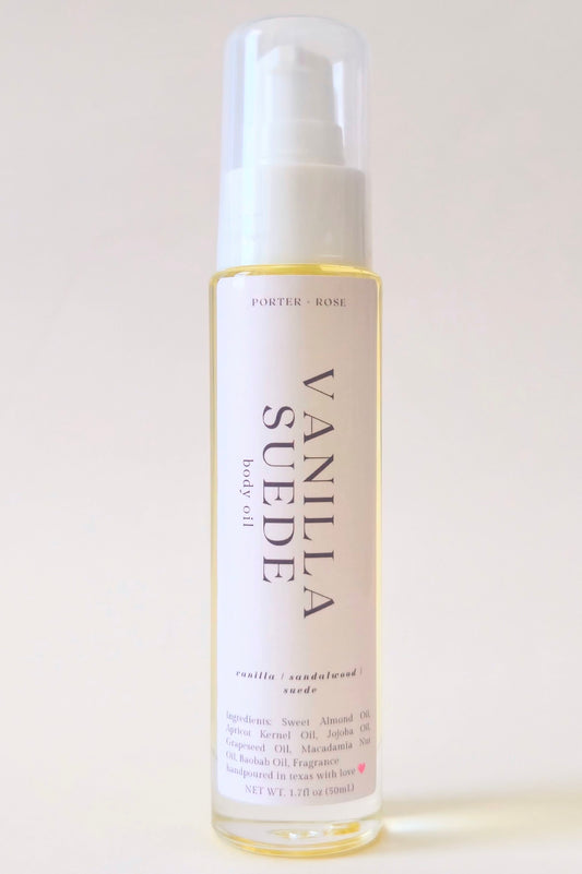 A bottle of Porter Rose Vanilla Suede body oil with a white spray cap and a cream-colored label, set against a plain off-white background.